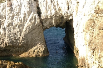 The white arch. A geological feature where the pale white rock of the cliff outcrop has been worn away by the sea to create an archway above, and a channel through to a shallow semi enclosed area of water.