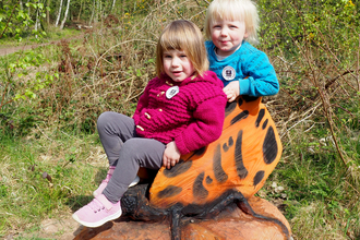 Two small children sitting on a wooden sculpted butterfly