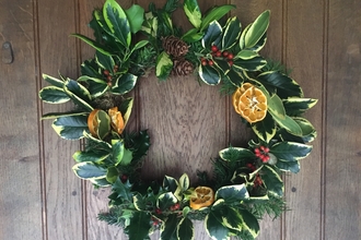 A handmade Christmas wreath, with holly and other evergreen leaves, dried orange slices, bright red berries, and pinecones. 