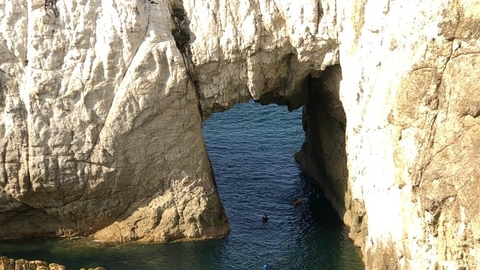 The white arch. A geological feature where the pale white rock of the cliff outcrop has been worn away by the sea to create an archway above, and a channel through to a shallow semi enclosed area of water.