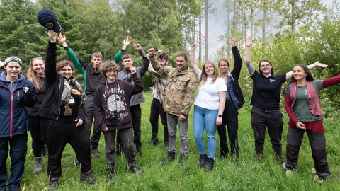 A group of young people pose for a picture in front of woodland