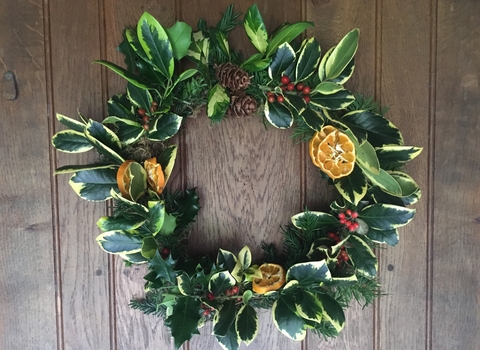 A handmade Christmas wreath, with holly and other evergreen leaves, dried orange slices, bright red berries, and pinecones. 